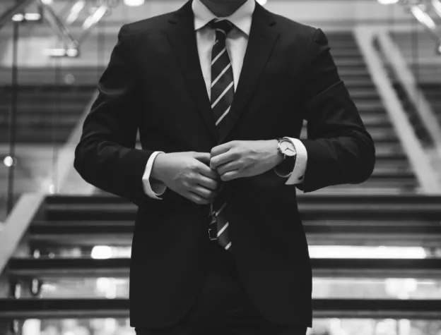 A well-dressed man in a suit and tie stands on stairs