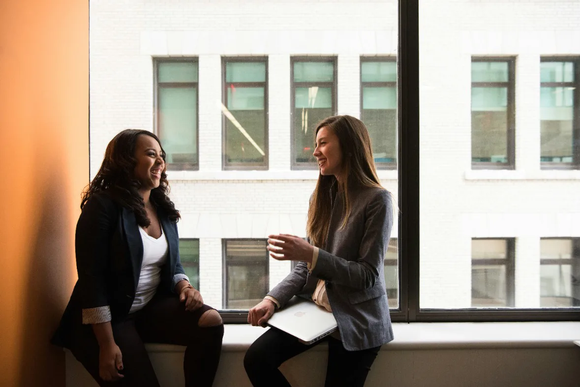 Two women engaged in a discussion by a window,
