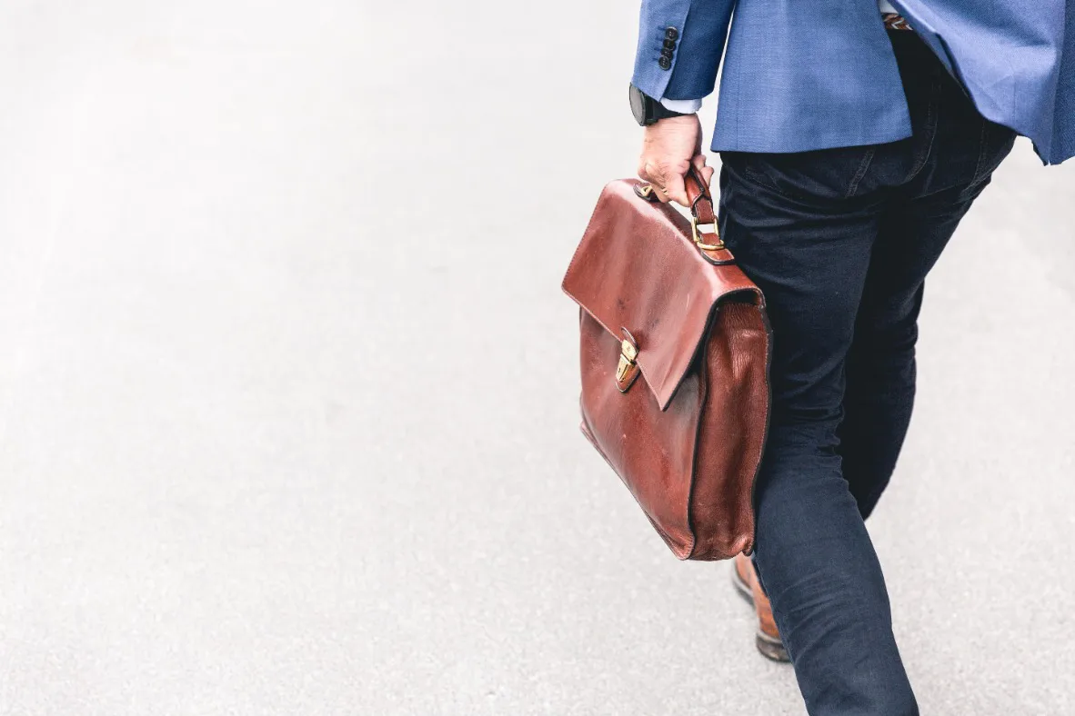 A man in a suit and tie walks confidently while carrying a briefcase in his right hand.