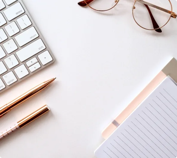  A black and white image of a desk featuring a keyboard, glasses, and a notepad