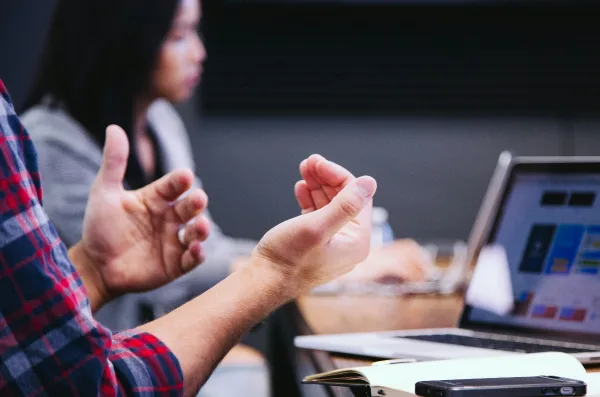 A man gestures while seated at a desk with a laptop, symbolizing engagement in real estate ownership solutions.