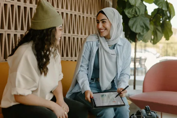 Two women seated on a couch, engaged with a tablet, symbolizing connection and collaboration in a modern setting.