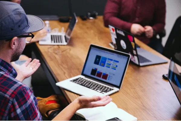 A man seated at a table, working on his laptop, symbolizing focus and productivity in a professional environment.