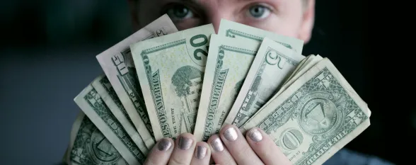 A woman holds a stack of money in front of her face