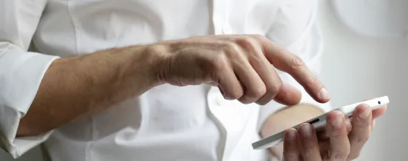 A man wearing a white shirt is holding a cell phone, seemingly interacting with it or checking messages.