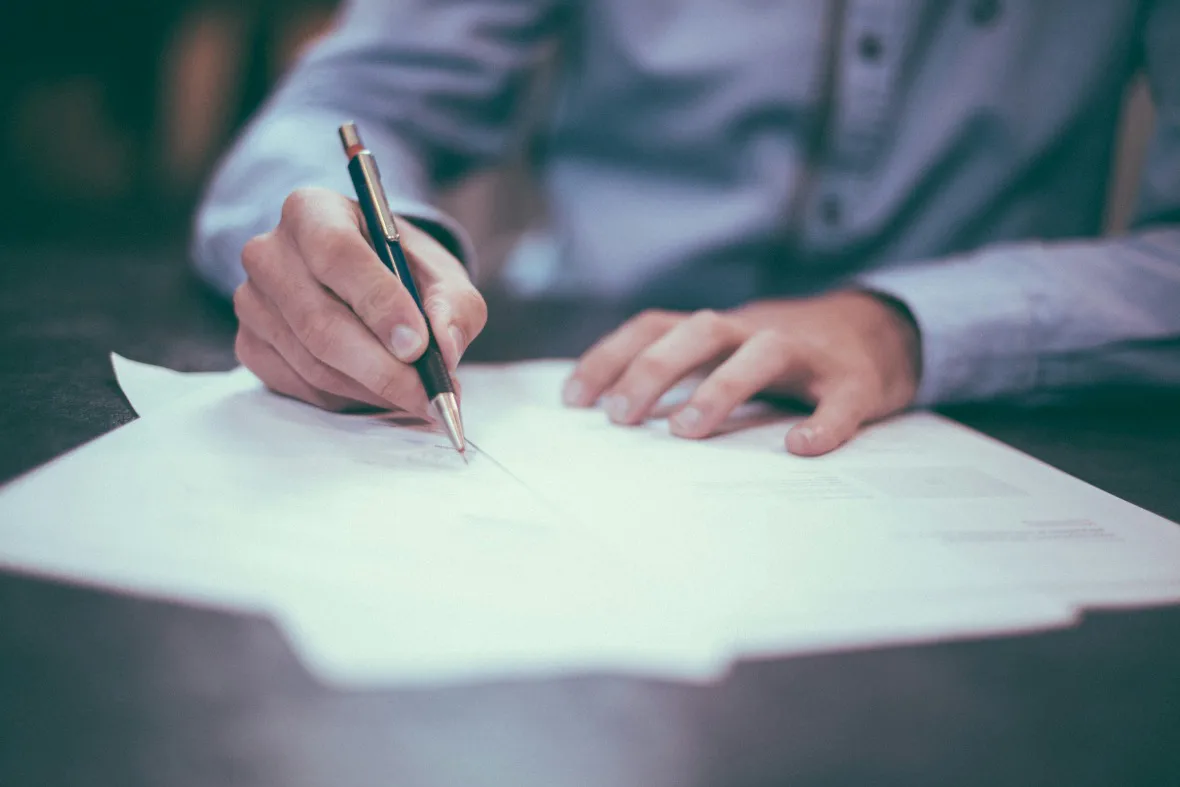 A person in a professional setting, carefully writing on paper with a pen